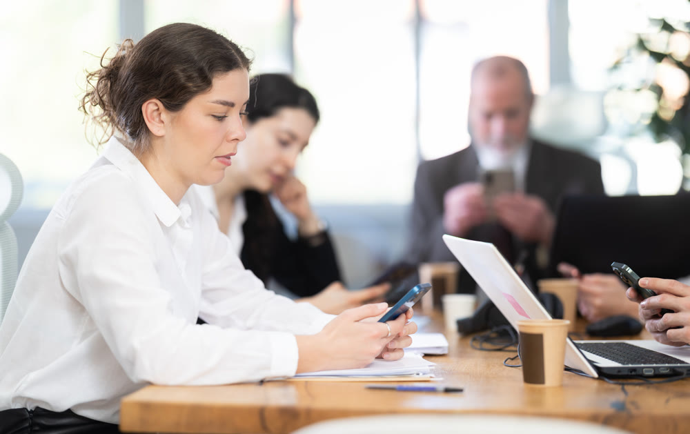 Woman scrolls through her smartphone while working in office with colleagues