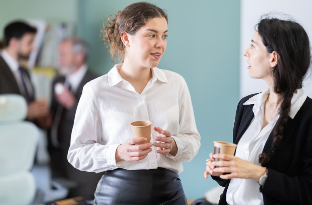 Two girls colleagues chat and laugh during coffee break
