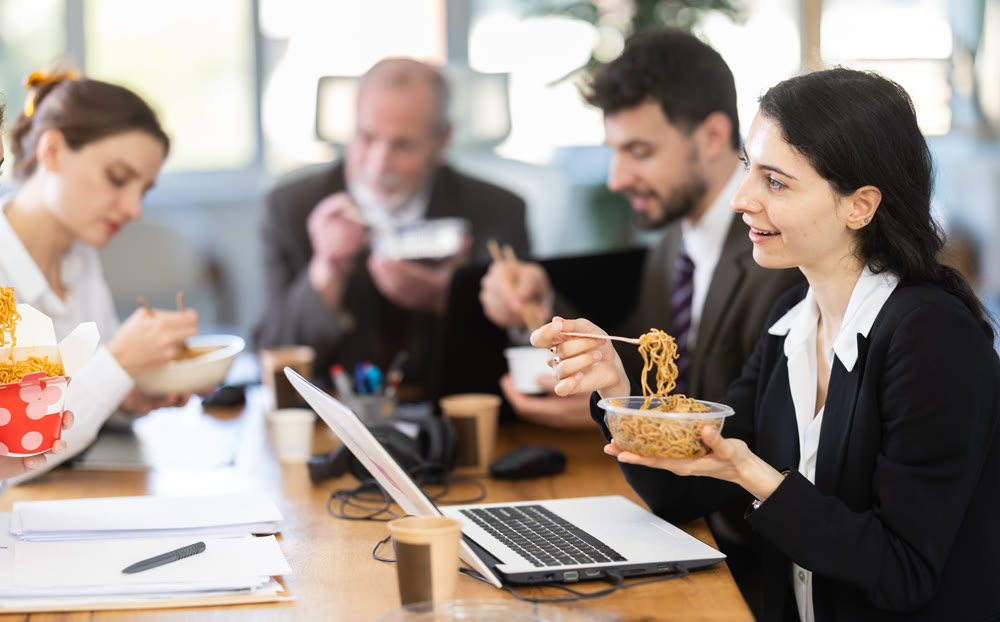 Lunch break - woman eating noodles with colleagues in modern office