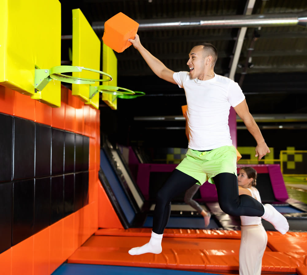 Athletic people throw ball into basketball basket while jumping on trampolines at an entertainment center