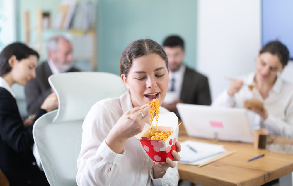 Lunch break - woman eating noodles with colleagues in modern office