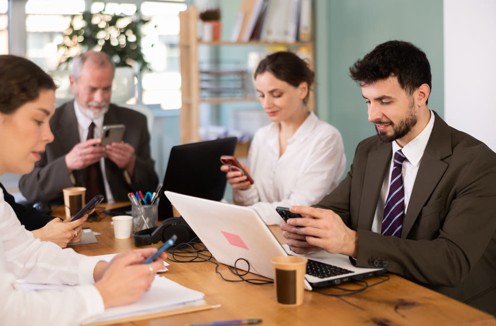 Team of managers look at smartphone screens while working in modern office