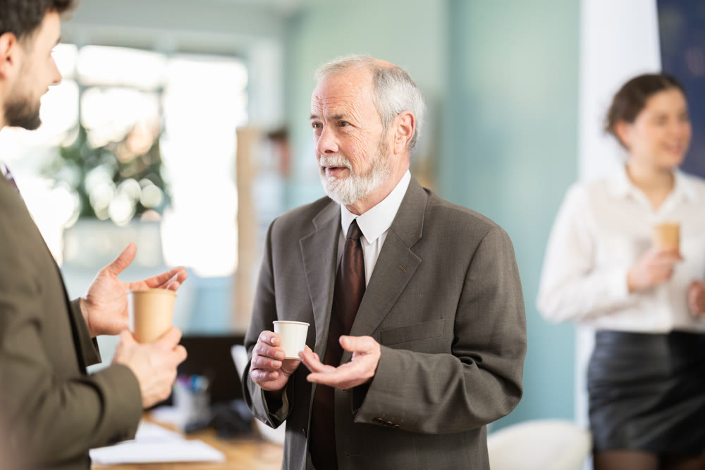 Two man co-workers employees drinking hot coffee and talking during break while working in office