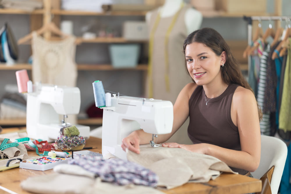 Female clothing designer stitching fabric on sewing machine in studio