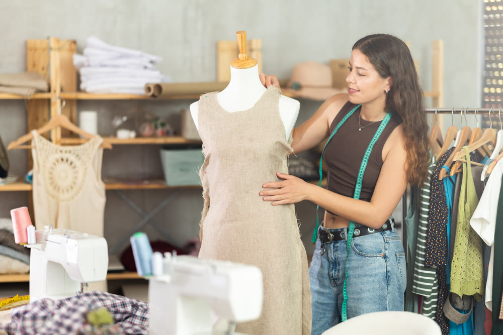 Female fashion designer sewing dress and testing it on mannequin