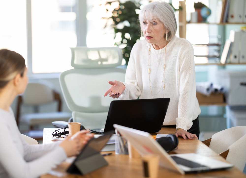 Elderly woman scolding female colleague working on tablet