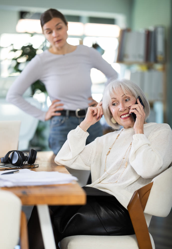 Adult woman judging female colleague talking on mobile phone