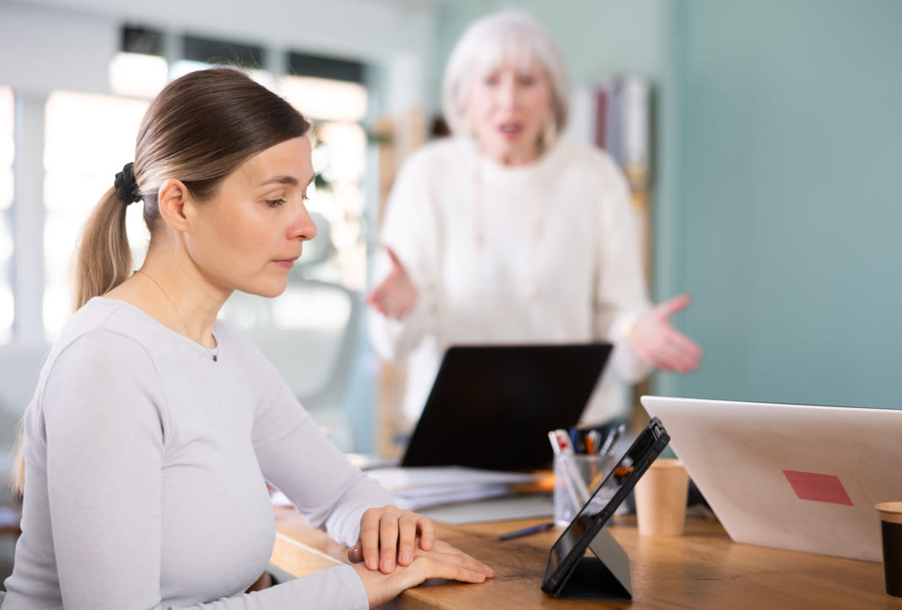 Elderly woman scolding female colleague working on tablet