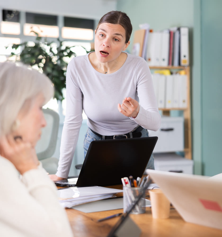 Adult woman scolding female colleague working on tablet