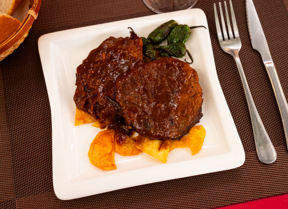 Veal roast with black sauce garnished by French fries and decorated baked green peppers.