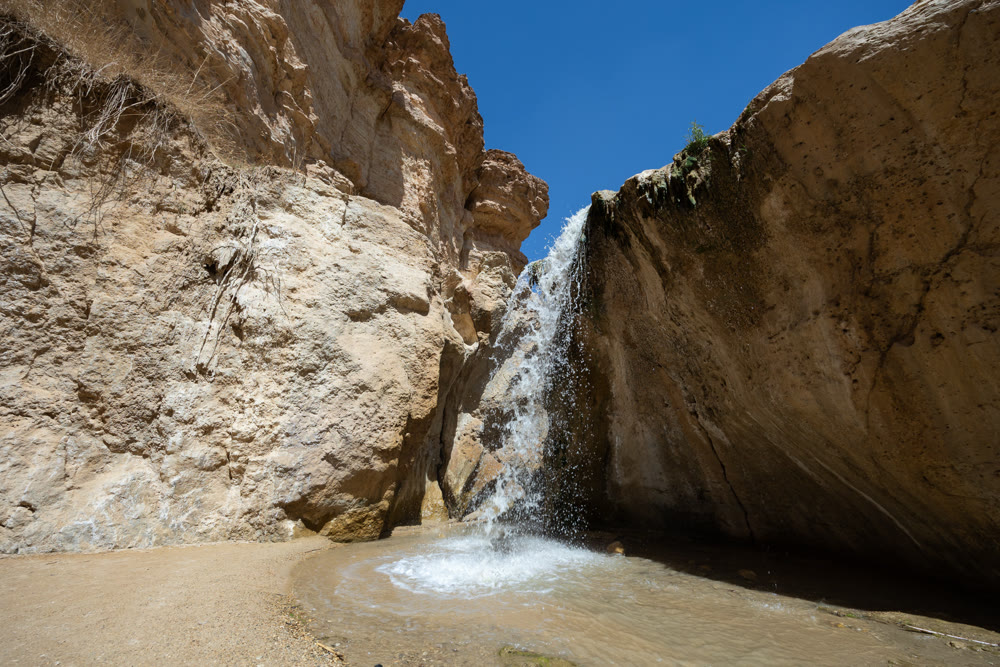 Small waterfall cascading into serene pool within oasis of Tamaqzah, Tunisia, surrounded by rugged cliffs