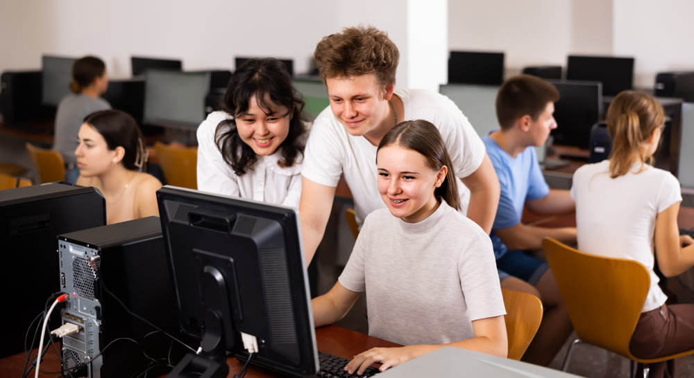 Portrait of multinational young students group emotionally reacting while studying at pc in computer class