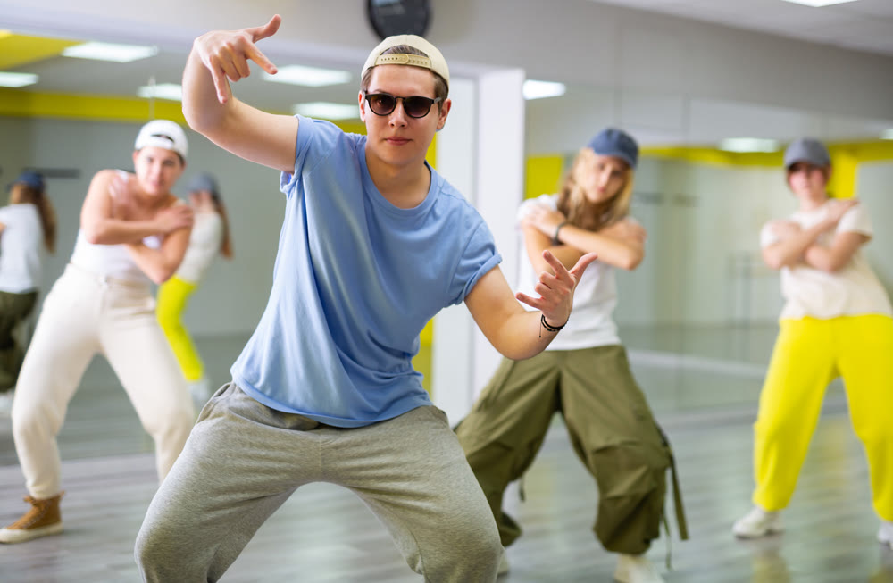Emotional teen boy dancing with group of friends in dance studio. Hip hop generation