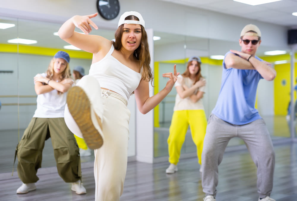 Ordinary teen girls and boy performing kick step movement during training together in dance school