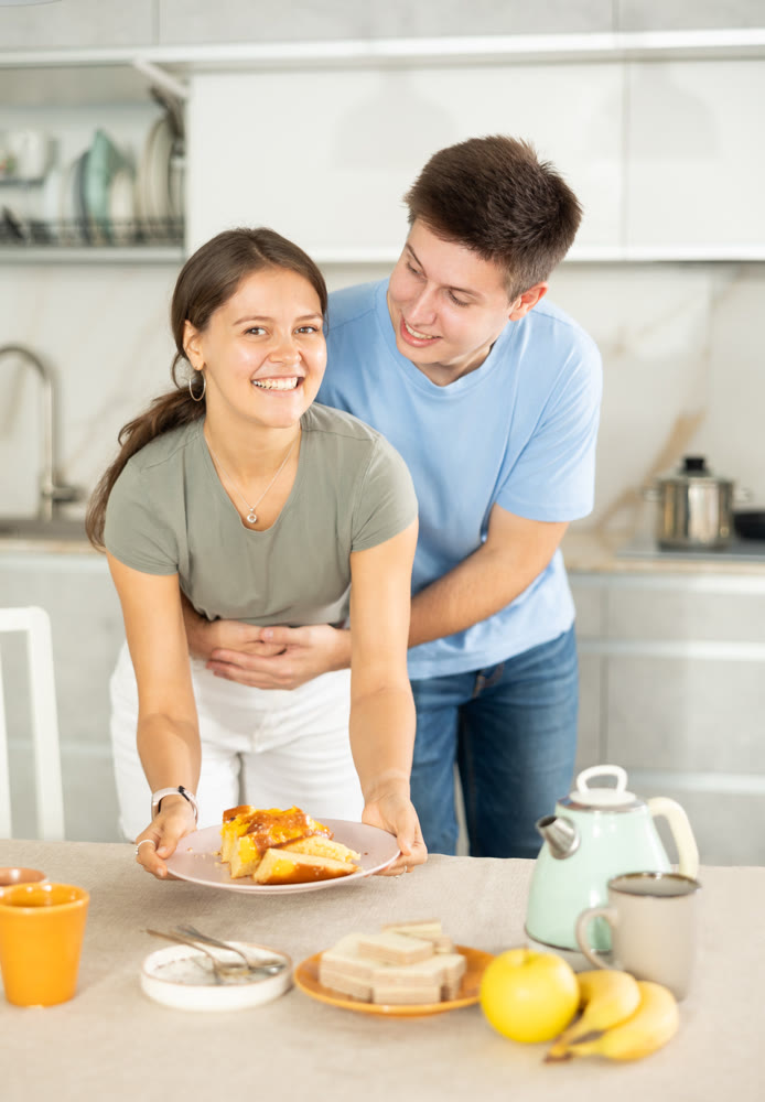 Guy gently hugs girlfriend around waist during preparations for afternoon snack
