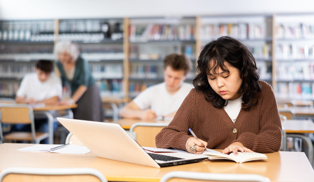 Schoolgirl studies on a laptop and writes notes in a copybook