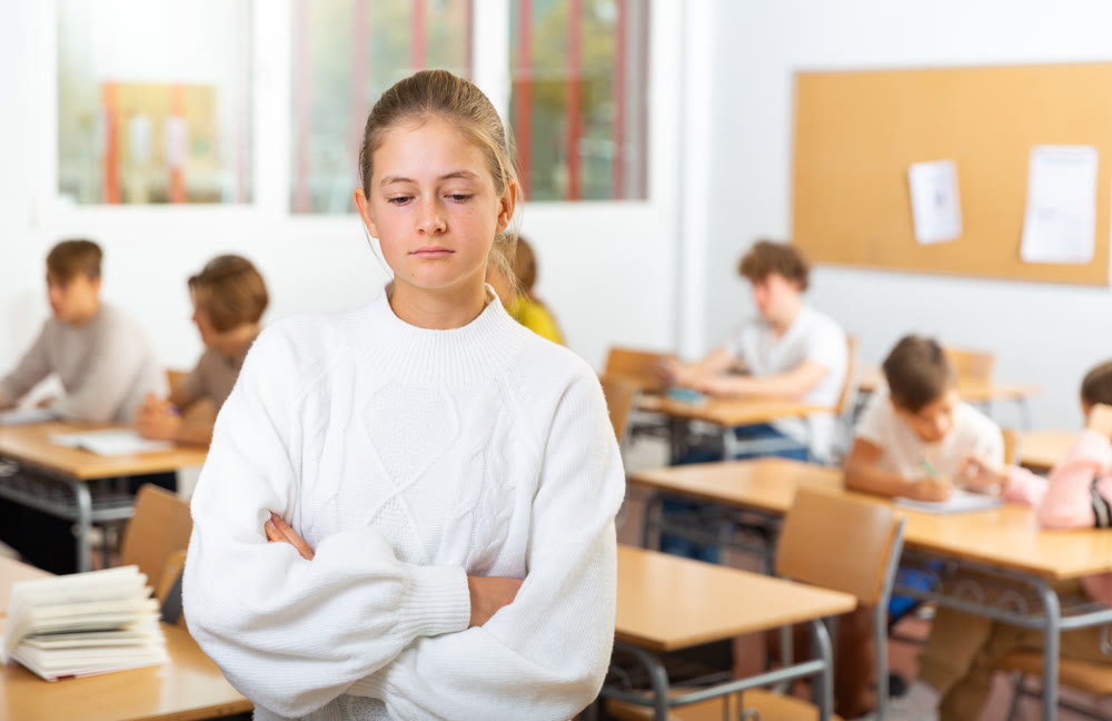 Upset girl stands in a school class against background of classmates