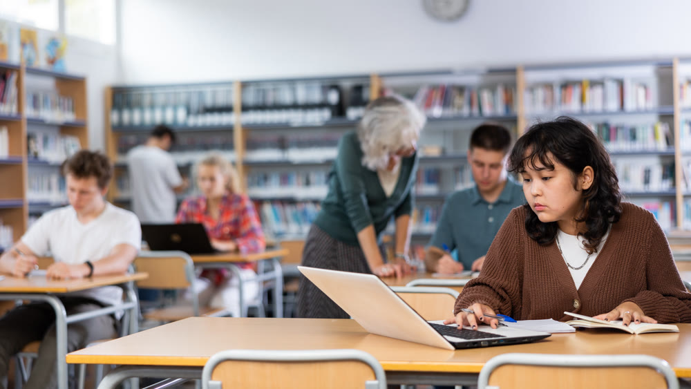 Asian teenager girl with a laptop studying in school library