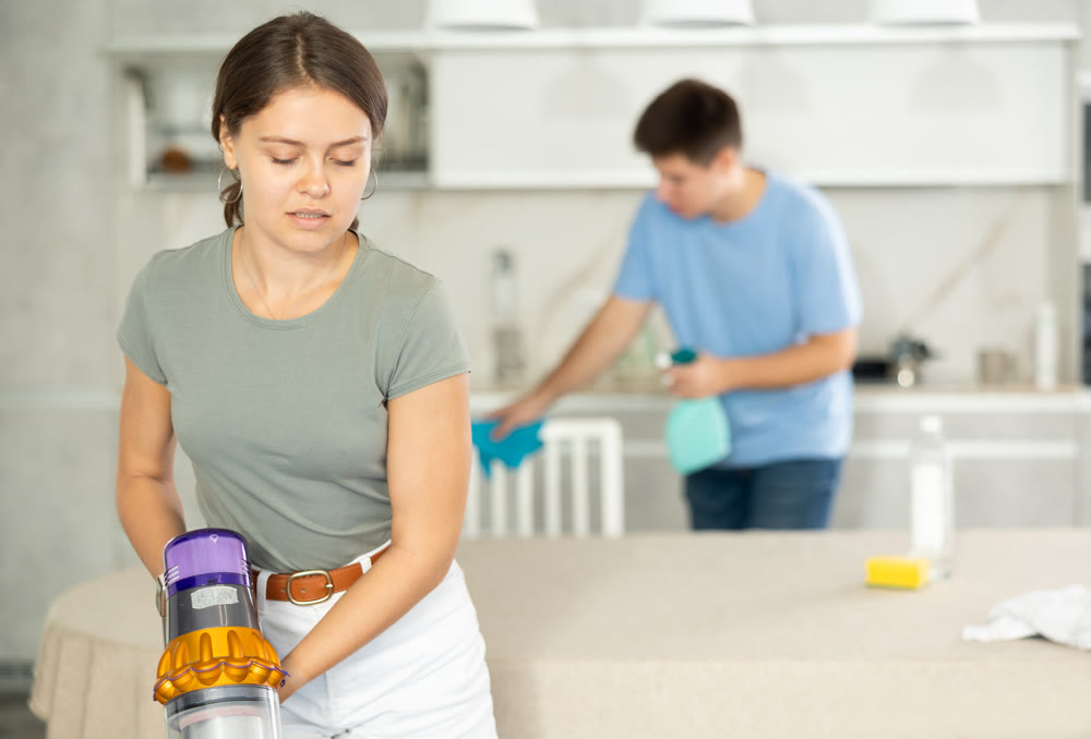 Girl collects dust with vacuum cleaner during group cleaning in kitchen
