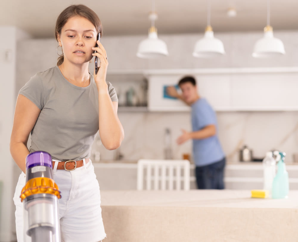 Girl cleans kitchen with vacuum cleaner and has nice conversation on phone with her friend