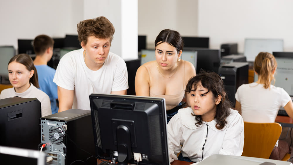Serious students explaining the topic to female friend while she is studying computer science on the PC in the classroom
