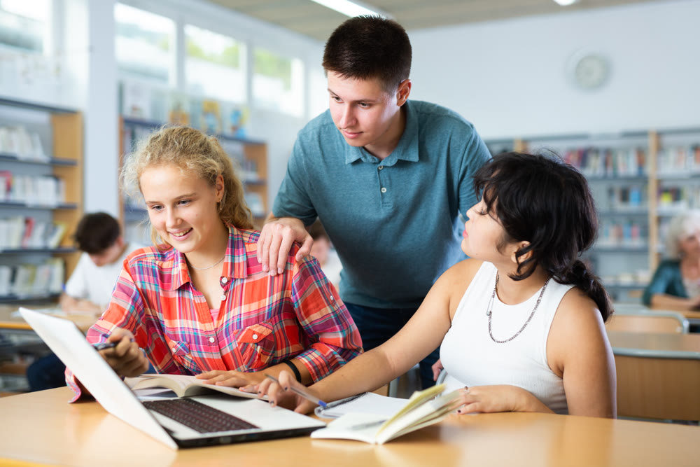 Three schoolchildren are studies on a laptop and taking abstracts in a copybook