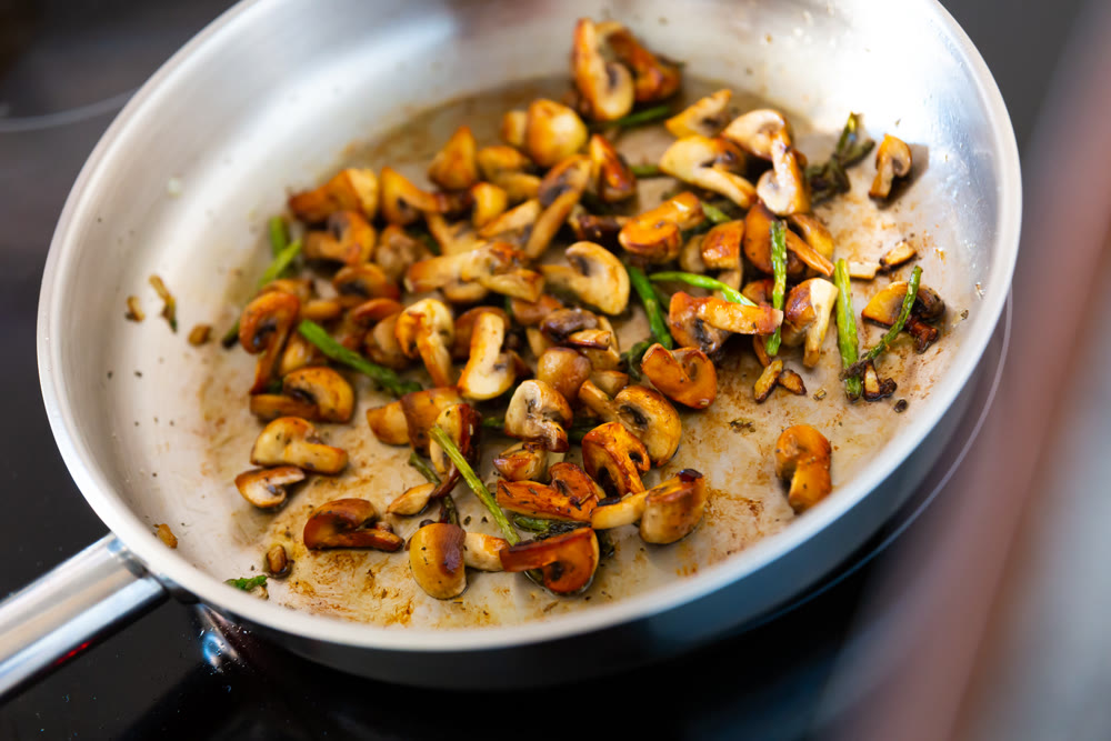 Finely chopped champignons and young asparagus shoots are fried in frying pan.
