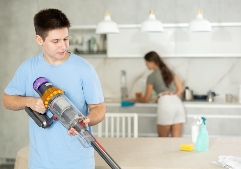 Guy collects dust with vacuum cleaner during group cleaning in kitchen