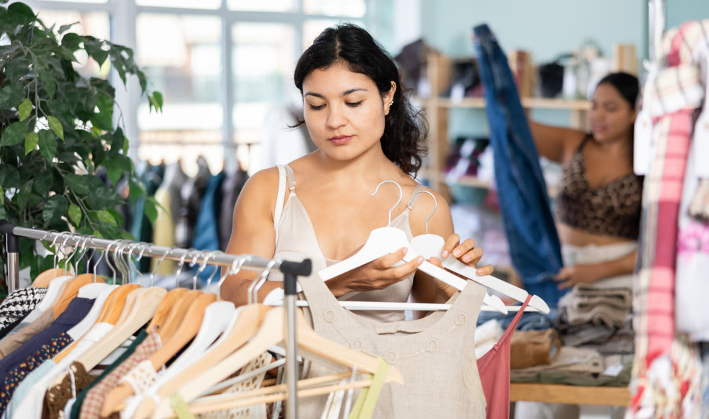 Selective young girl choosing summer dresses or tops in clothing store