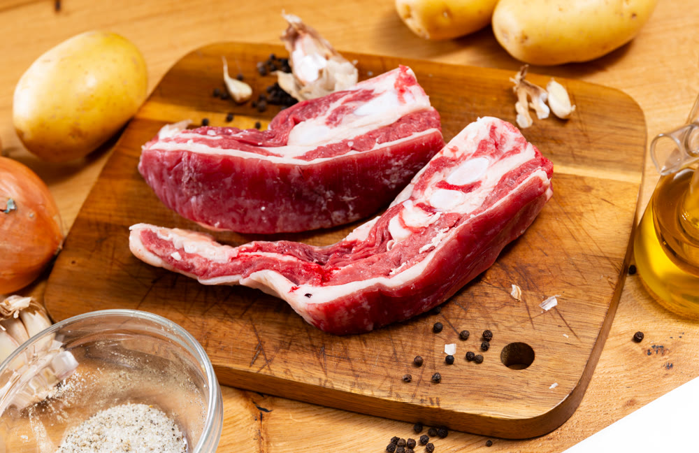 Raw beef ribs on board, potato tubers and whole onions