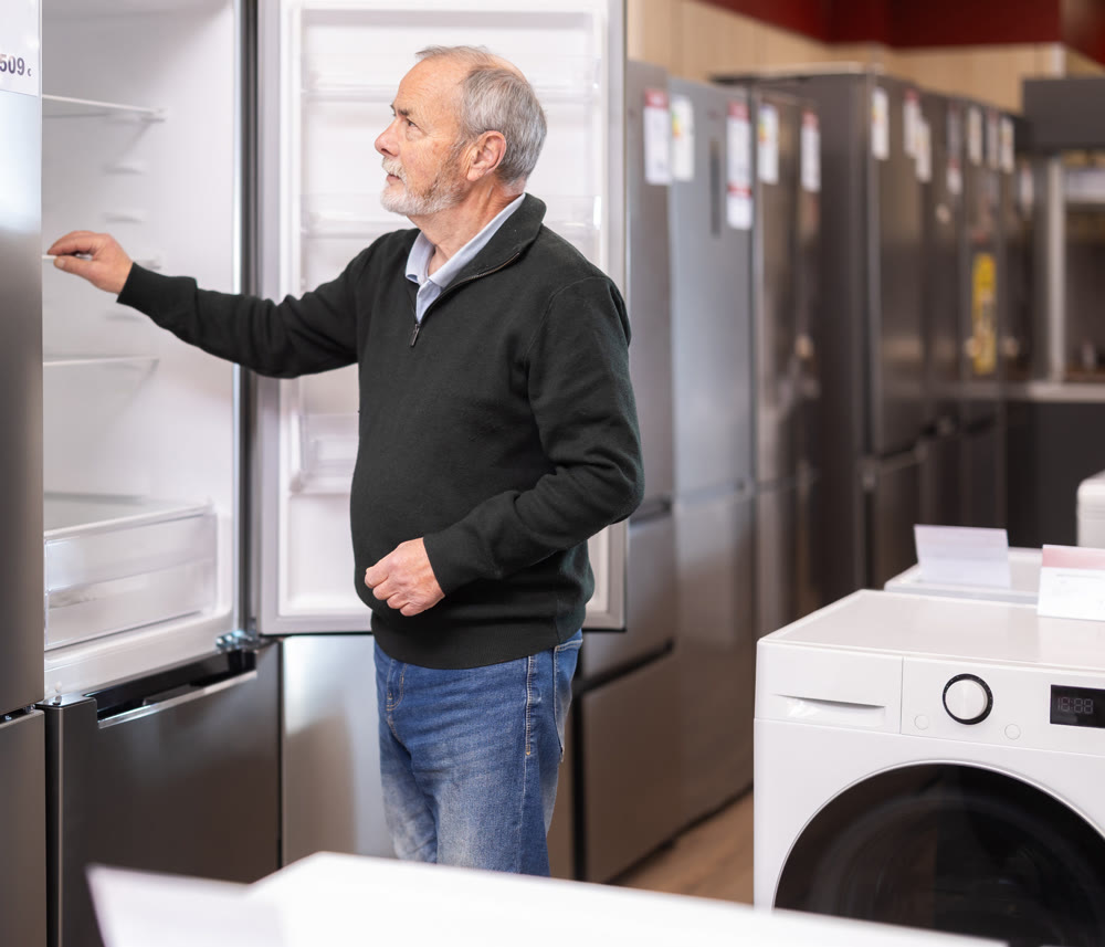 Elderly man choosing a large refrigerator in a store