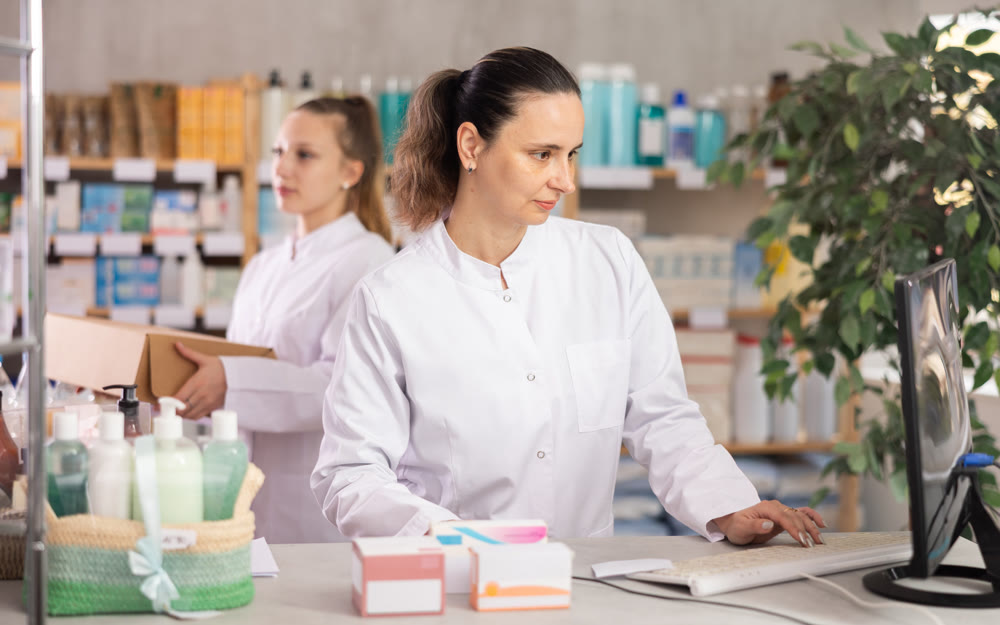 Female pharmacist searches for information about medicines on the Internet, while the assistant places medicines on display