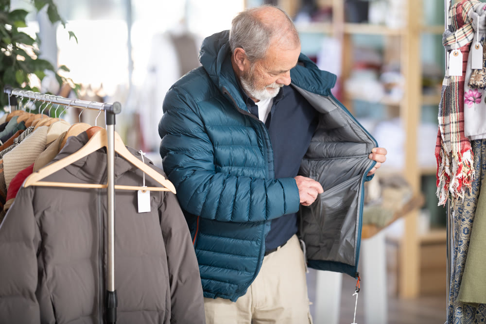 Mature male customer is trying on down jacket during shopping in store
