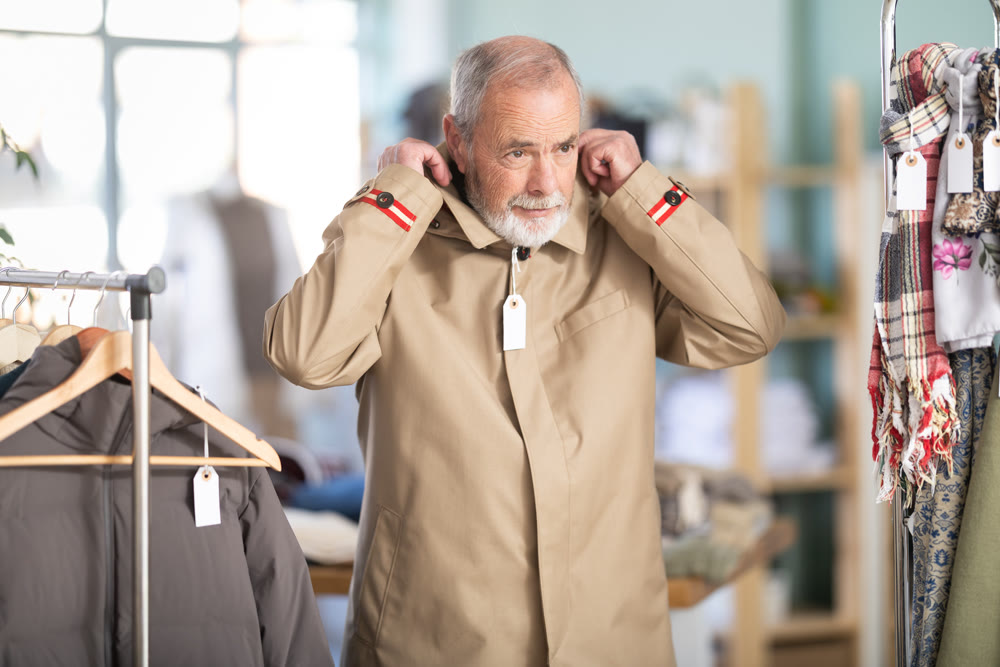 Mature male customer is trying on raincoat during shopping in store