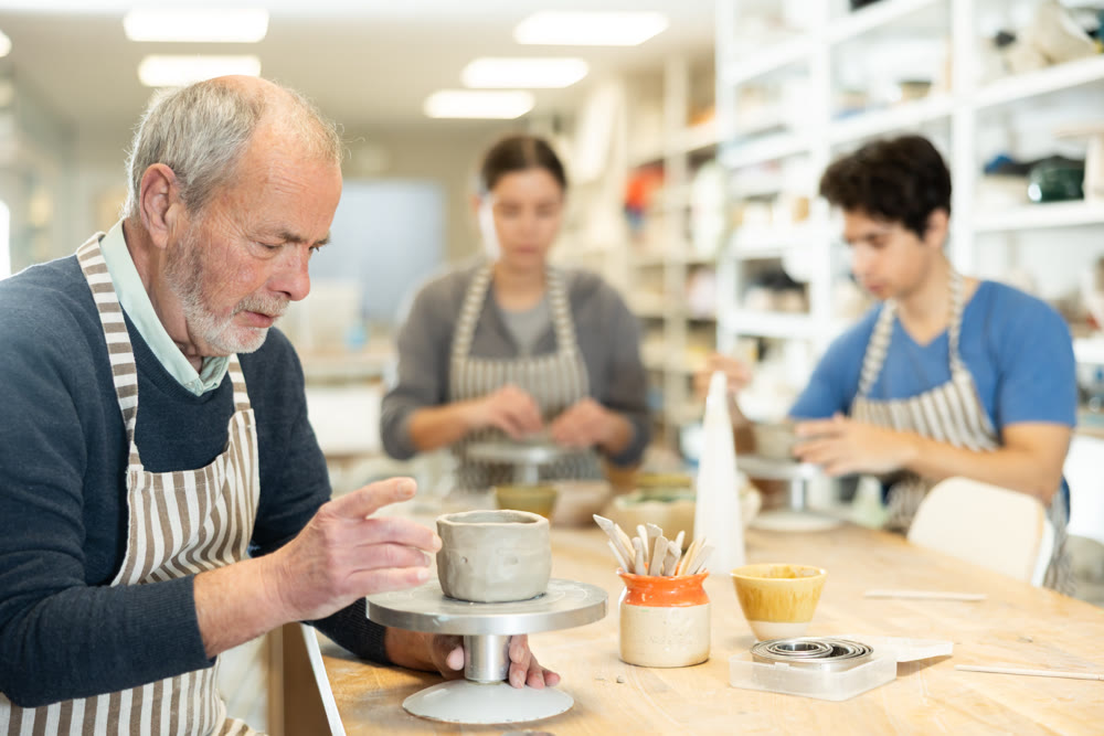 Mature man at table molds cup from wet clay in pottery workshop