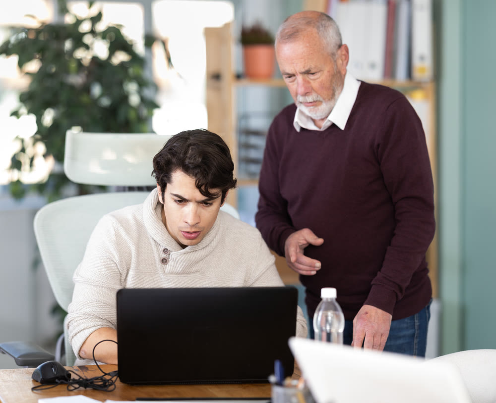 Mature male manager helping to guy during working at laptop in office