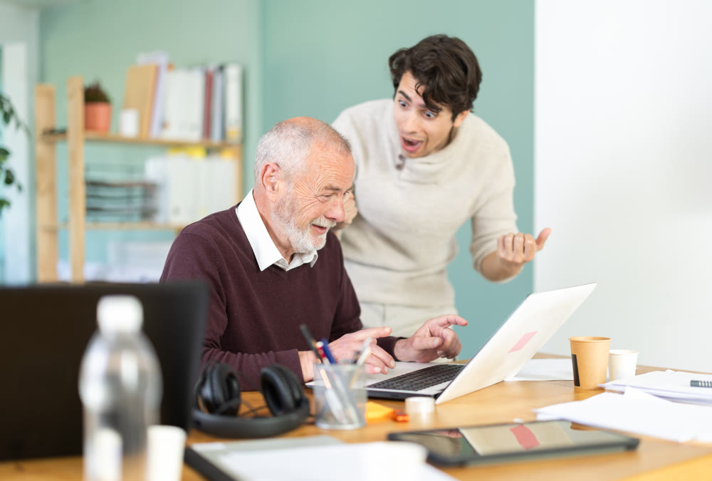Happy young and elderly men colleagues cheering at successful result on laptop