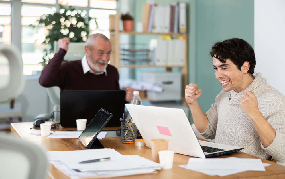 Happy young and elderly men colleagues cheering at successful result on laptop