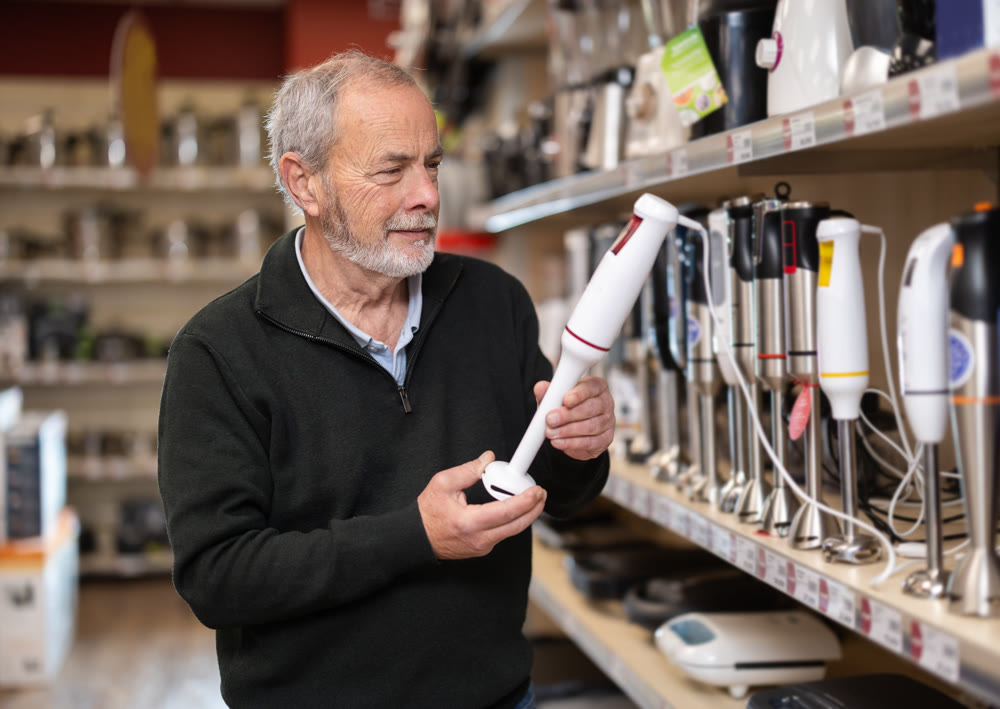 Elderly man chooses electric blender at supermarket