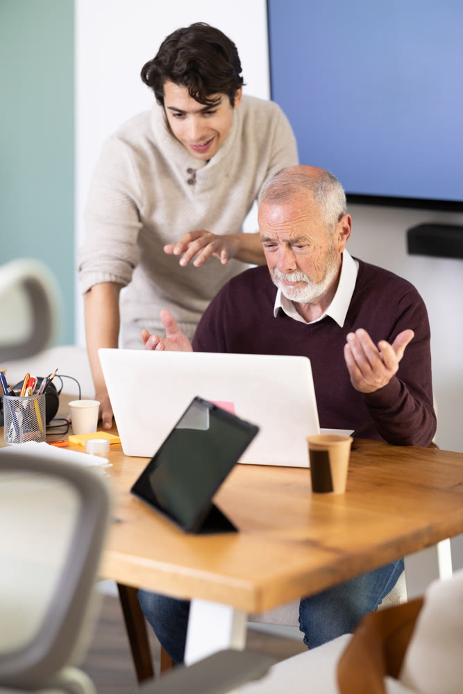 Guy helps elderly man complete task on laptop