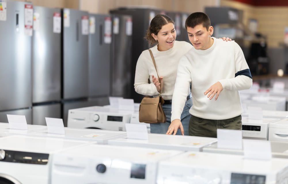Young couple chooses modern washing machine or dishwasher at hypermarket