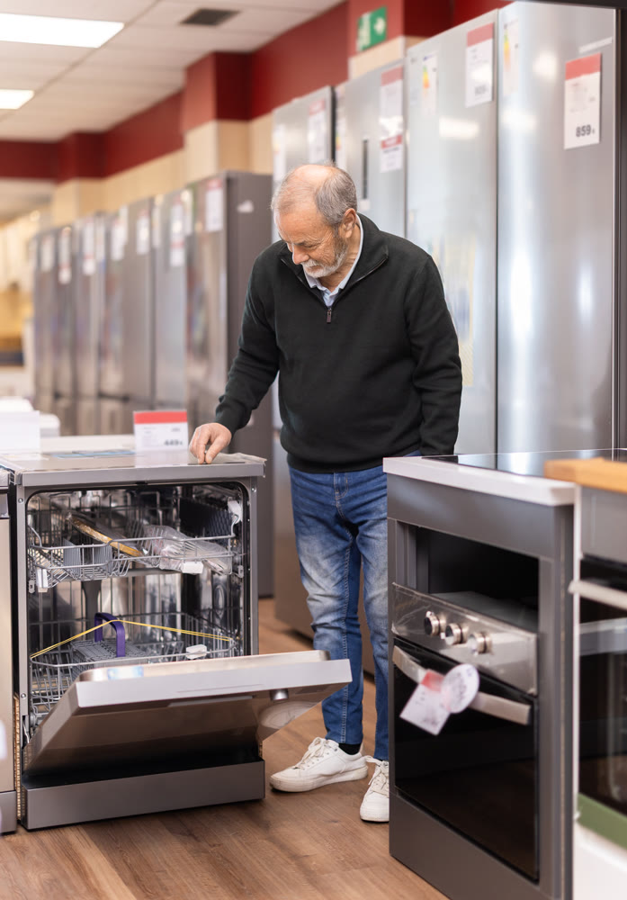 elderly man chooses a washing machine and a dishwasher in a store