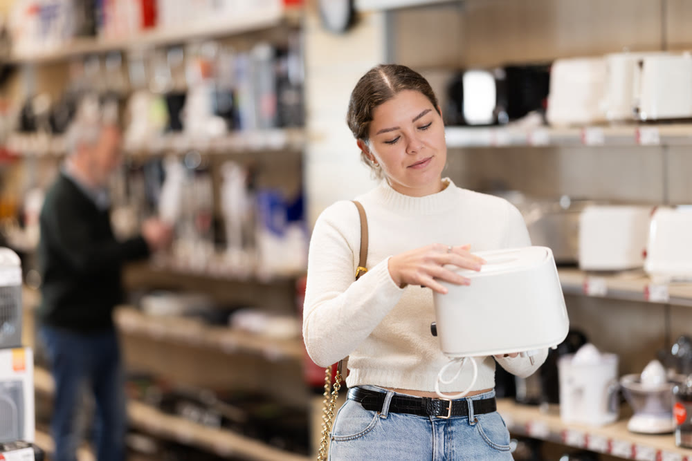 Positive young woman choosing toaster in hypermarket