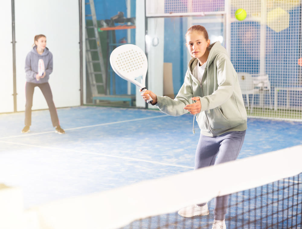 Active teen girl playing padel on tennis court