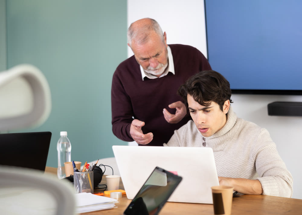 Mature male manager helping to guy during working at laptop in office