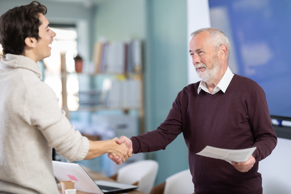 Young and elderly men shaking hands with documents in office