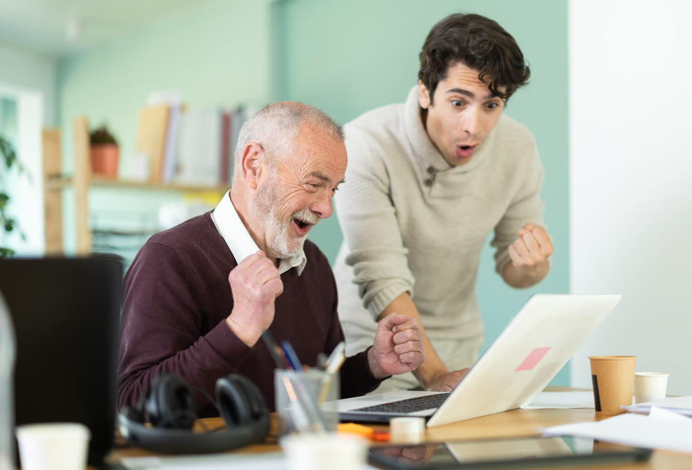 Happy young and elderly men colleagues cheering at successful result on laptop