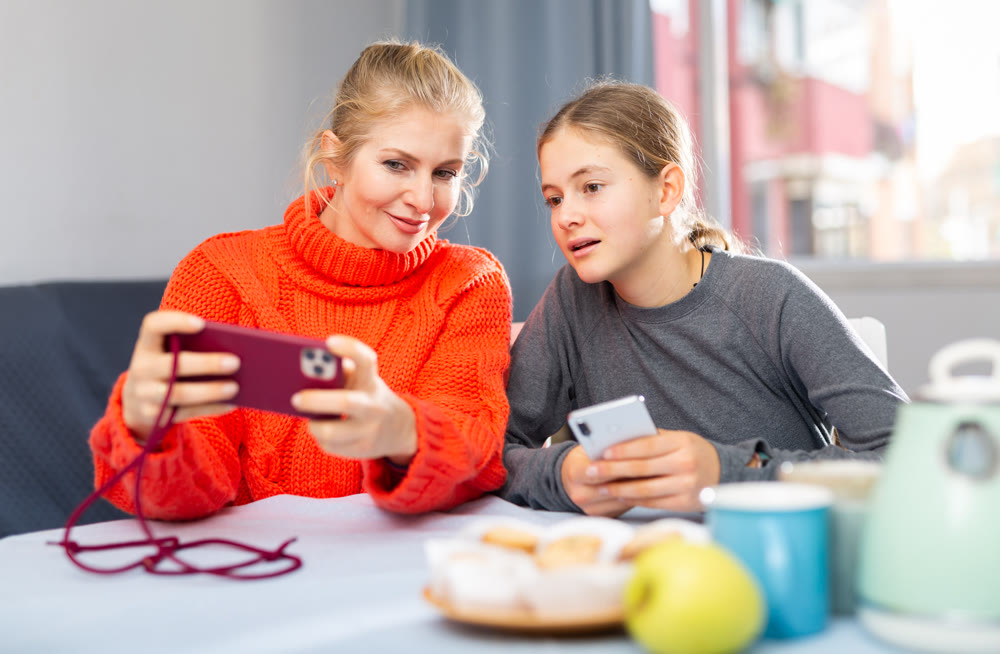 Mother and daughter together playing on their smartphones while sitting at table at home