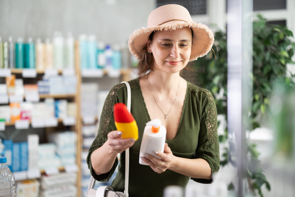 Woman in straw hat choosing sunscreen in pharmacy