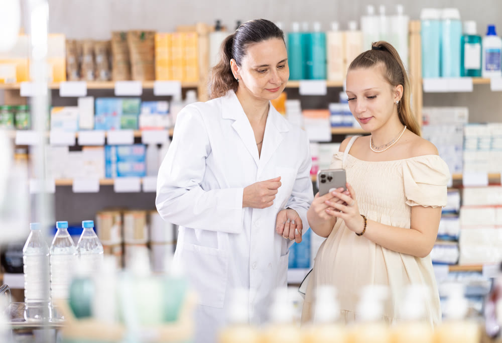 Pregnant woman with phone chooses medicines with help of pharmacist
